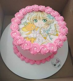 a pink cake decorated with an anime character on the front and sides, sitting in a cardboard box