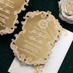 a wedding card with gold foil on it and a white rose next to it in front of an envelope