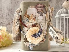 an altered book is sitting next to some flowers and a birdcage with music notes on it