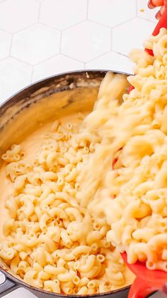 a pot full of macaroni and cheese being stirred with a red spatula