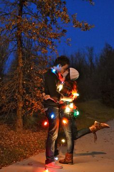 a man and woman standing next to each other on a sidewalk covered in christmas lights