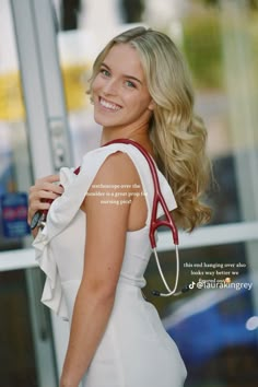 a woman in a white dress is holding a red purse and smiling at the camera