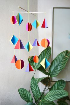 an origami mobile hanging on a wall next to a potted plant with text overlay that reads diy geometric paper mobile