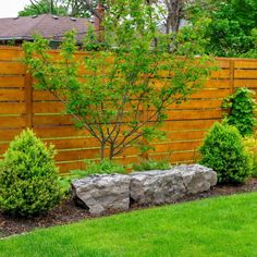 a wooden fence in the middle of a yard with trees and bushes on either side