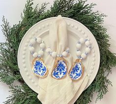 a white plate topped with two blue and white dishes next to a green wreath filled with pine branches