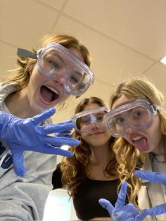 three girls wearing goggles and gloves making funny faces with their hands in the air