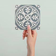 a hand holding up a square tile with an intricate design