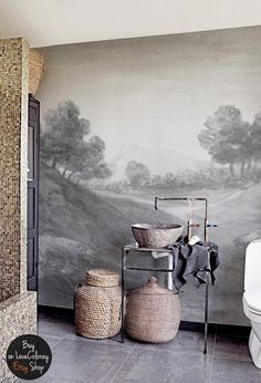 a bathroom with a large mural on the wall next to a toilet and trash can