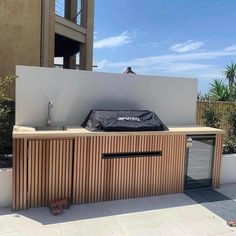 an outdoor bbq with grilling equipment on the side of it and a building in the background