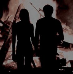 two people standing next to each other in front of a fire