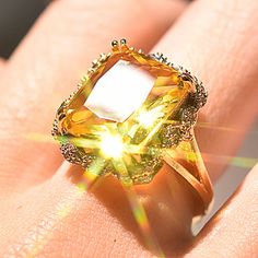 a woman's hand with a yellow diamond ring on top of her finger and the sun shining through it