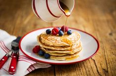 pancakes with berries and syrup being poured onto them