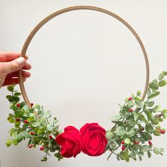 a hand holding a hoop with flowers and greenery