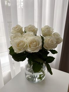 a glass vase filled with white roses on top of a table