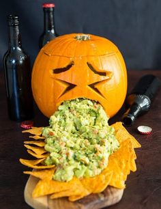 a carved pumpkin sitting on top of a wooden table next to some chips and bottles