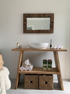 a wooden table with baskets under it and a mirror on the wall above it, next to a white sink