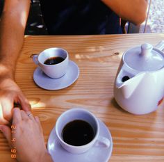 two people are sitting at a table with cups of coffee and one is holding the hand of another person