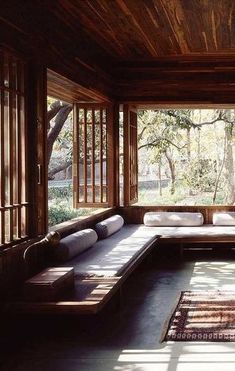 a living room filled with lots of windows and wooden furniture on top of a rug