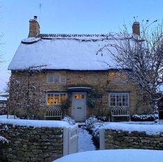 a stone house covered in snow next to a fence and tree with no leaves on it