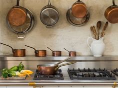 pots and pans are hanging on the wall above an oven with cooking utensils