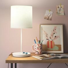 a desk with a lamp, bowl and pictures on the wall next to each other