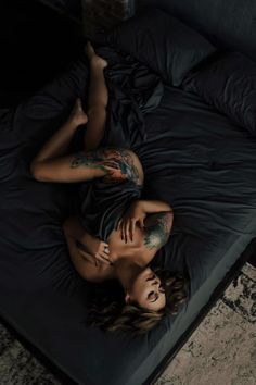 two beautiful women laying on top of a bed in a room with black sheets and pillows