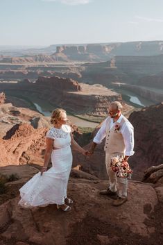 a bride and groom holding hands on top of a cliff overlooking the grand canyons