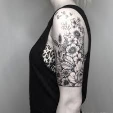 a woman with a flower tattoo on her arm and shoulder, standing in front of a gray wall