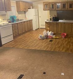 an empty kitchen and living room with wood flooring in the foreground, white appliances on the far wall