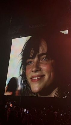 a woman is smiling while standing in front of a large screen with the image of herself on it