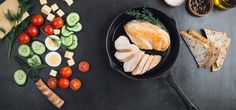 a pan filled with sliced chicken and vegetables next to bread, tomatoes, cucumbers, crackers and olives