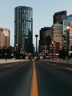 an empty city street with tall buildings in the backgroud and lights on either side