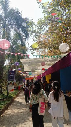 many people are walking down the street with kites hanging above them and trees in the background