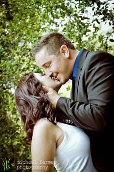 a man and woman kissing in front of trees