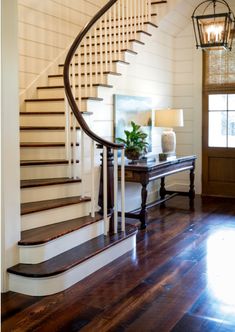 a foyer with a wooden floor and stairs leading up to the second floor, along with a lamp on an end table