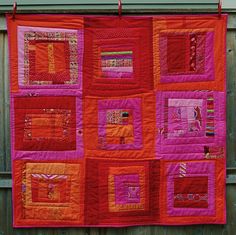 an orange and pink quilt hanging on a wooden fence