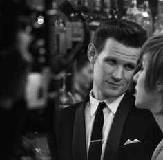 a man and woman standing next to each other in front of a bar filled with liquor bottles