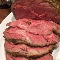 a white plate topped with sliced meat on top of a wooden table