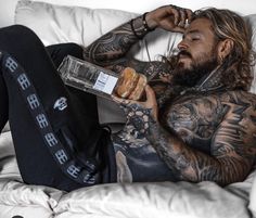 a tattooed man sitting on top of a white couch holding a box of doughnuts