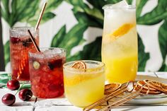 three glasses filled with drinks sitting on top of a white tiled counter next to fruit