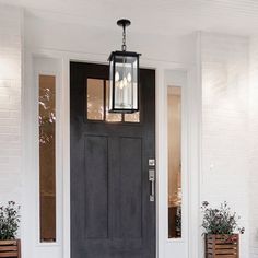 a black front door with two planters and a light hanging from the ceiling above it