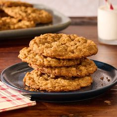 three oatmeal cookies stacked on a plate next to a glass of milk