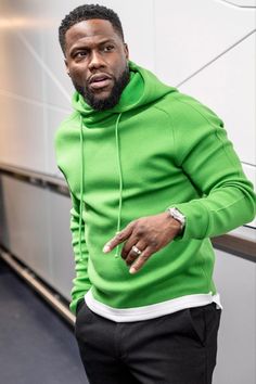 a man in a green hoodie pointing to the side with his hand on his hip