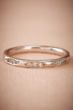 a white gold wedding ring with three diamonds on it's side, sitting on a beige surface