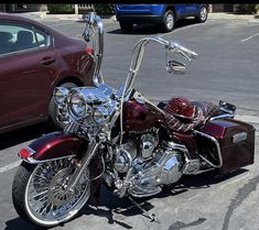 a maroon motorcycle parked in a parking lot next to a red car on the street