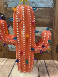 a ceramic cactus with colorful beads on it's back and arms, sitting on a wooden table