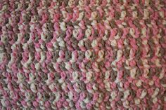 a crocheted pink and brown blanket on top of a bed