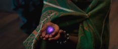 a person holding a small purple object in their left hand and wearing a green shawl