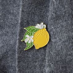 a pin with a lemon on it sitting on top of a gray sweater, next to a white flower and green leaf