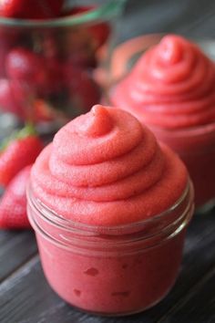 two jars filled with red colored food sitting on top of a table next to strawberries